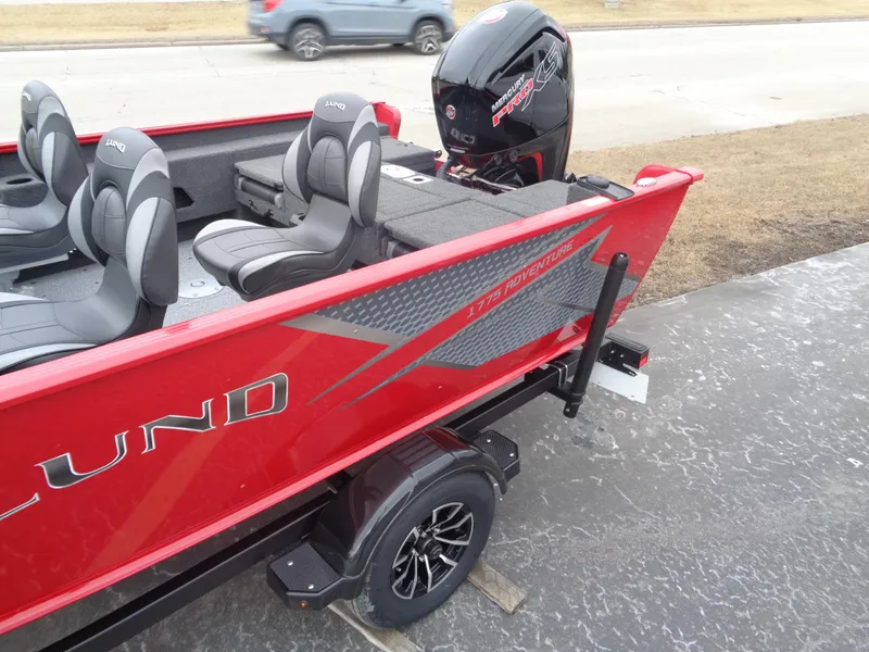 Slide: The Image of 2025 Lund 1775 Adventure Sport boat, red exterior, black motor, parked on pavement. - 5