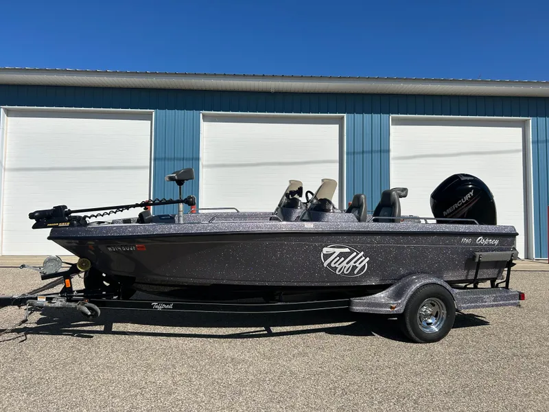 Slide: The Image of 2014 Tuffy 1760 Osprey fishing boat on trailer, parked outside blue building. - 16
