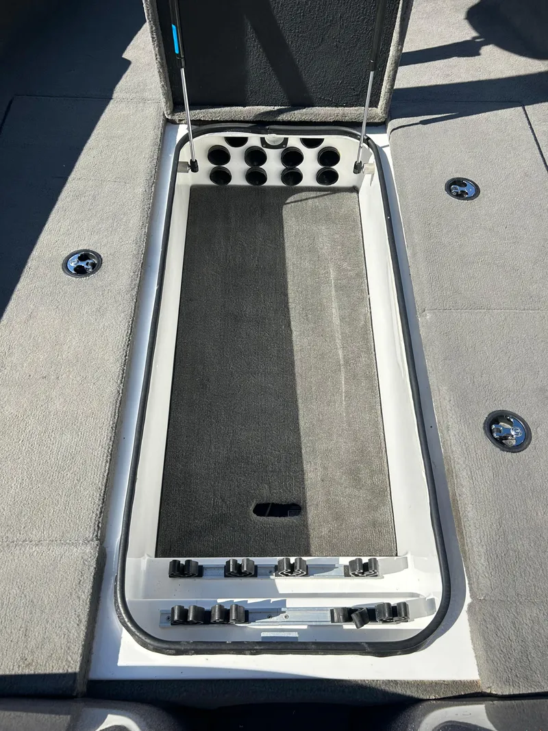 Slide: The Image of 2014 Tuffy 1760 Osprey boat storage compartment with rod holders and carpeted interior. - 36