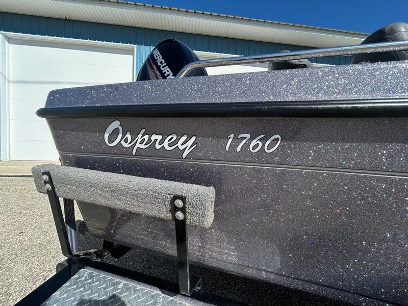 Slide: The Image of 2014 Tuffy Osprey 1760 boat with metallic finish, parked near a blue building. - 4