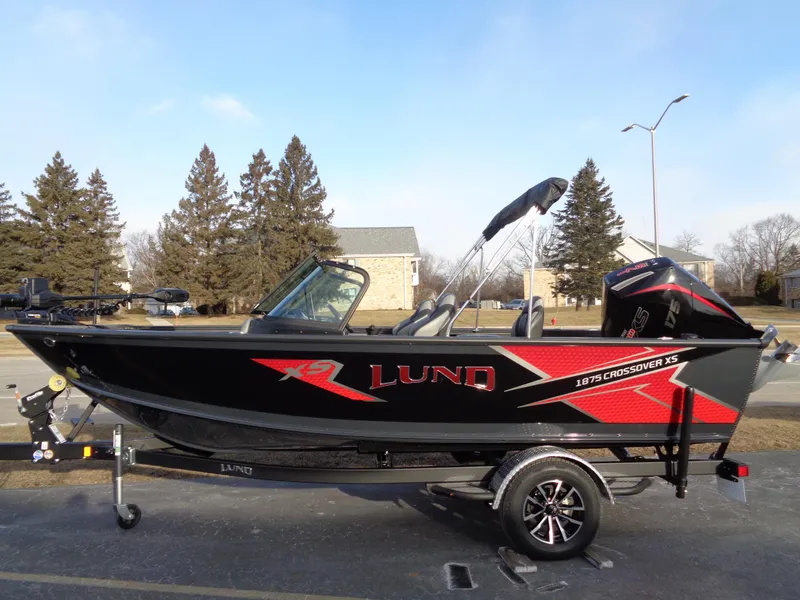 The Image of 2025 Lund 1875 Crossover XS boat, black and red design, parked outdoors. - 0