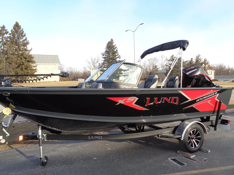 Slide: The Image of 2025 Lund 1875 Crossover XS boat, black with red accents, on a trailer. - 1