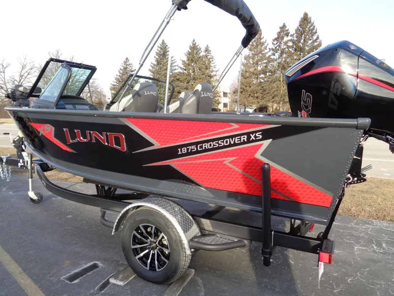 Slide: The Image of 2025 Lund 1875 Crossover XS boat with red and black design on a trailer. - 2