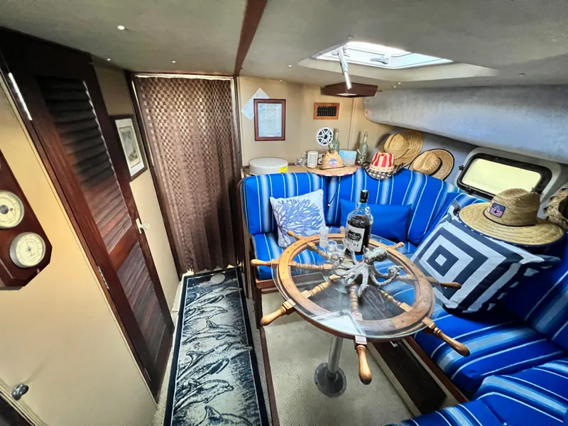 Slide: The Image of 1982 Silverton 37 Convertible interior with nautical decor, blue-striped seating, and a glass-top table. - 16