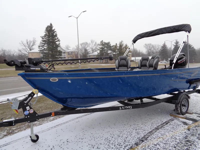 Slide: The Image of 2024 Lund 1650 Angler Tiller boat on trailer, blue exterior, snowy background. - 1