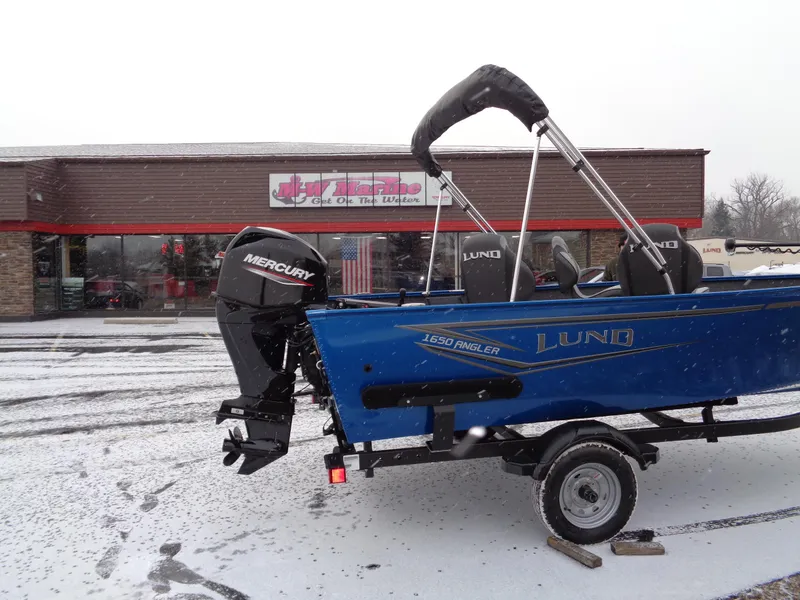 Slide: The Image of 2024 Lund 1650 Angler Tiller boat with Mercury engine in snowy parking lot. - 4
