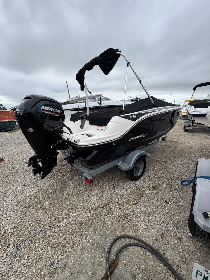The Image of 2023 Bayliner Element M17 boat with Mercury engine on a trailer, parked outdoors. - 1