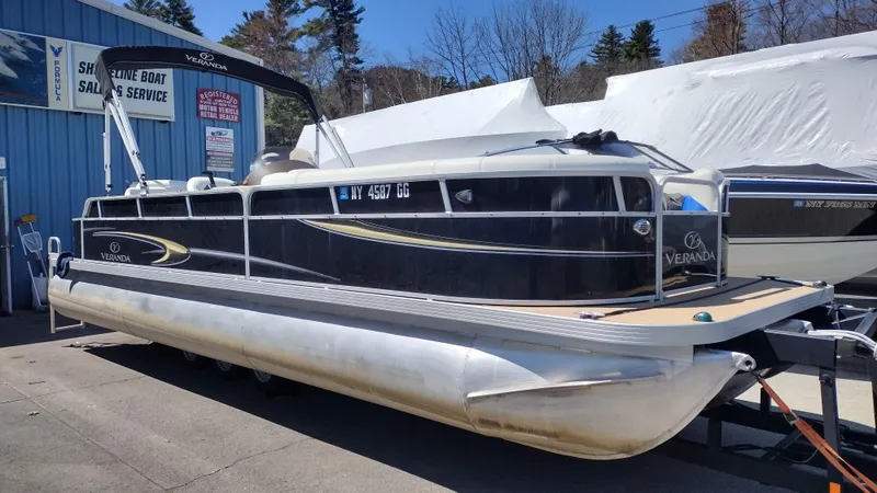 Slide: The Image of 2012 Veranda RFL2575V pontoon boat on trailer, parked near a boat sales and service shop. - 27