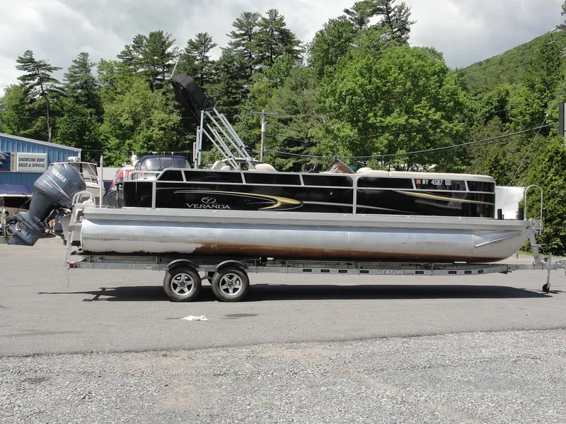 Slide: The Image of 2012 Veranda RFL2575V pontoon boat on trailer, parked outdoors with trees in background. - 6