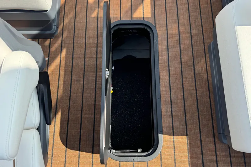 Slide: The Image of 2025 Manitou 24' Explore Switchback boat storage compartment with open lid on deck. - 10