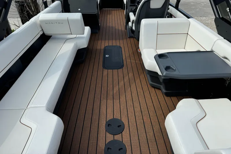 Slide: The Image of 2025 Manitou 24' Explore Switchback boat interior with sleek seating and wood-style flooring. - 6