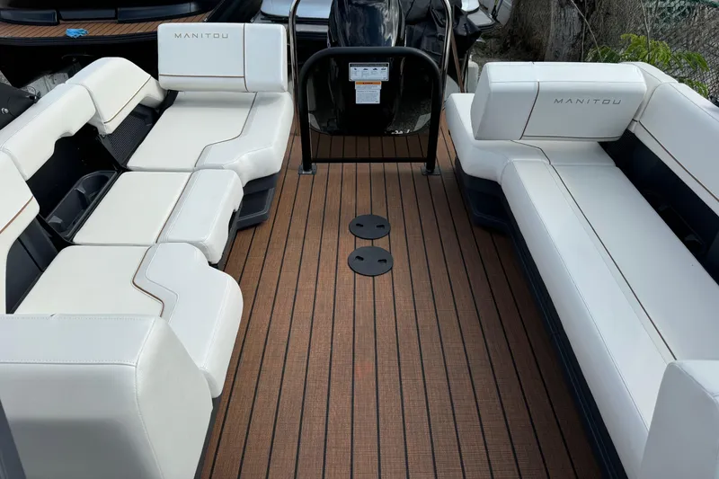Slide: The Image of 2025 Manitou 24' Explore Switchback boat interior with white seating and wood-style flooring. - 7