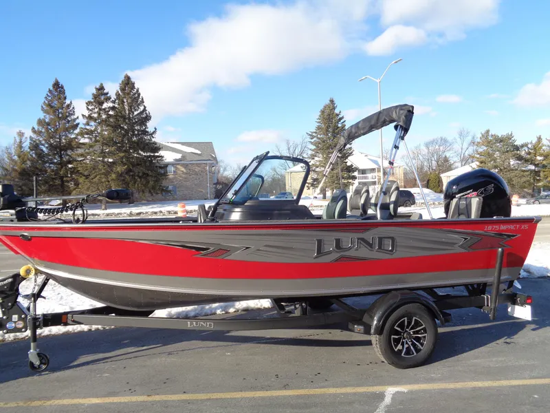 Slide: The Image of 2025 Lund 1875 Impact XS Sport boat, red and gray, parked on a trailer. - 1