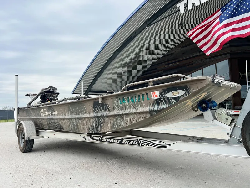 Slide: The Image of 2012 Pro-Drive 1854 boat on trailer, American flag, overcast sky background. - 5