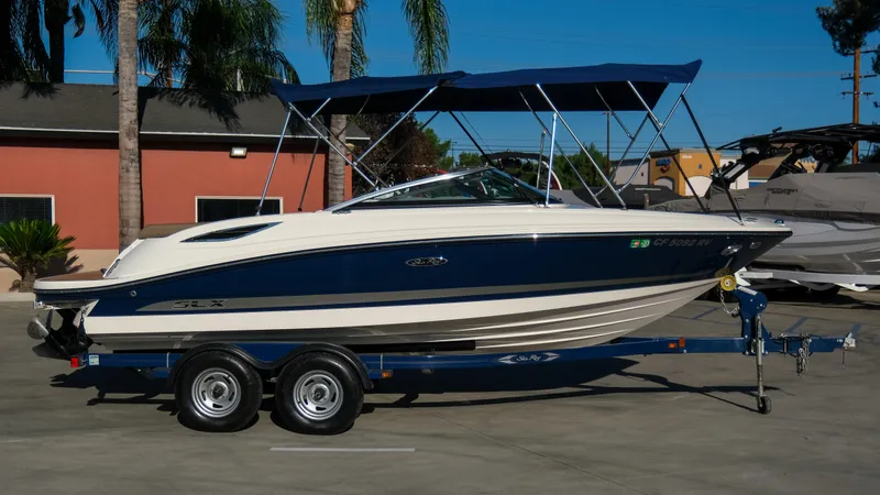 The Image of 2013 Sea Ray 210 SLX boat on trailer with blue canopy, parked outdoors. - 0