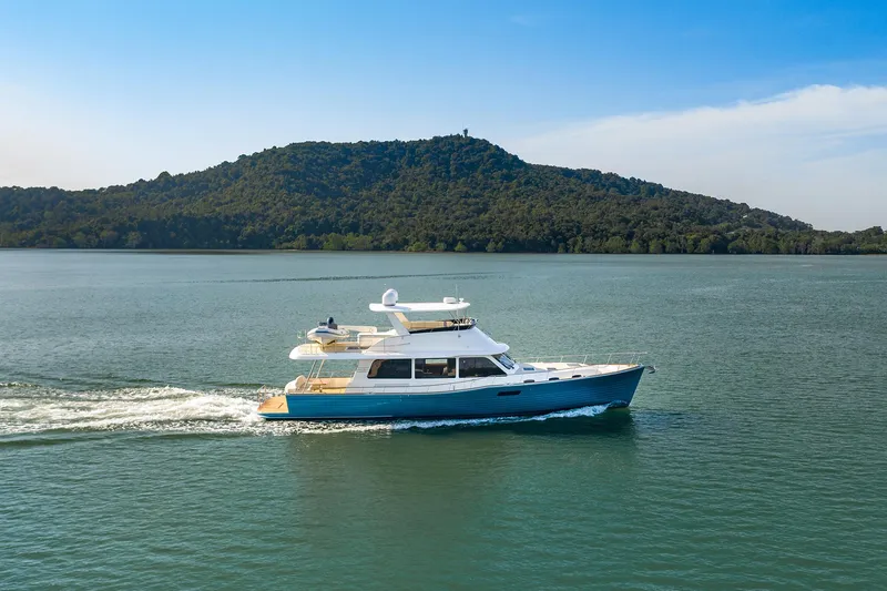 Slide: The Image of 2026 Grand Banks GB 60 yacht cruising on a serene lake with a forested hill backdrop. - 13