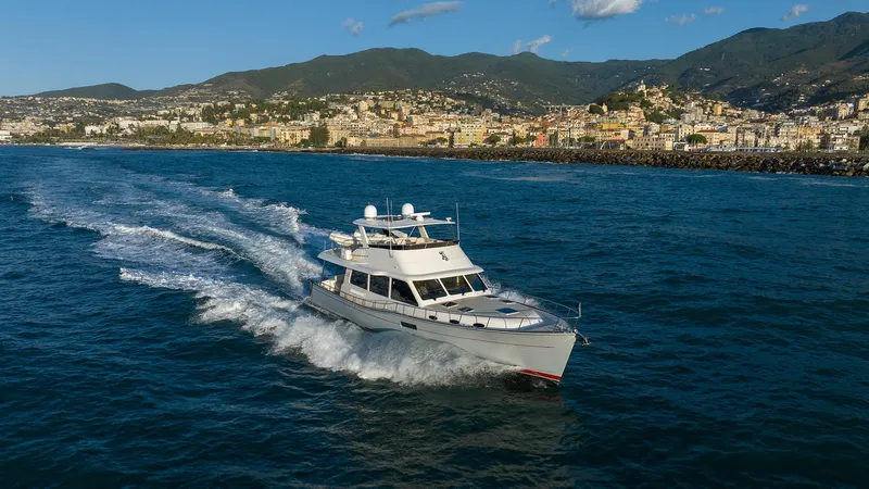 Slide: The Image of 2026 Grand Banks GB 60 yacht cruising on blue ocean near coastal cityscape. - 12