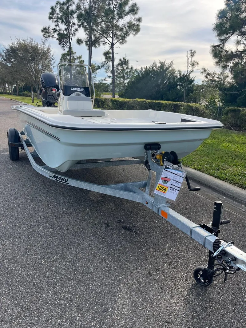 Slide: The Image of 2025 Mako Pro Skiff 17 CC boat on trailer, parked on a road with trees in background. - 3