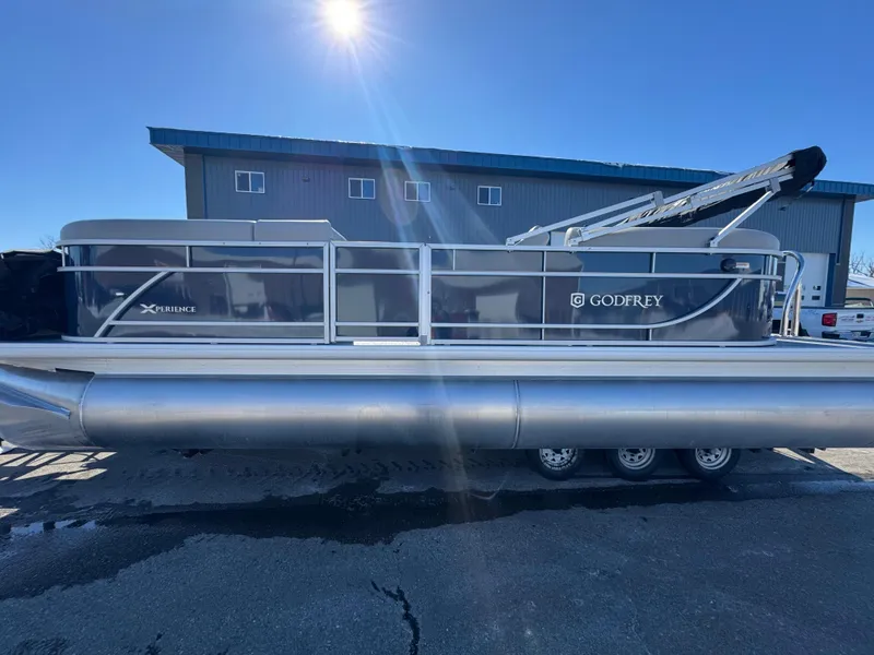 Slide: The Image of 2025 Xperience 2286 SBX pontoon boat under bright sunlight, parked near a building. - 2