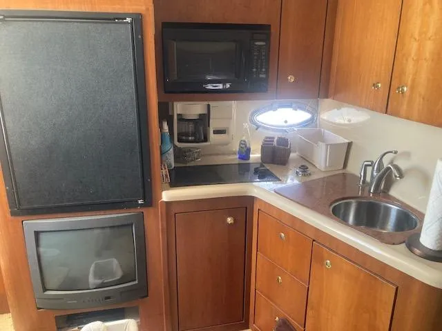 Slide: The Image of 2000 Cruisers Yachts 3575 Express kitchen with microwave, sink, and wooden cabinetry. - 13