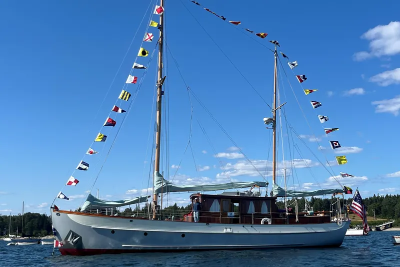 Slide: The Image of Classic 1938 Alden yacht with colorful flags, designed by Rockport Marine, sailing under a clear blue sky. - 19
