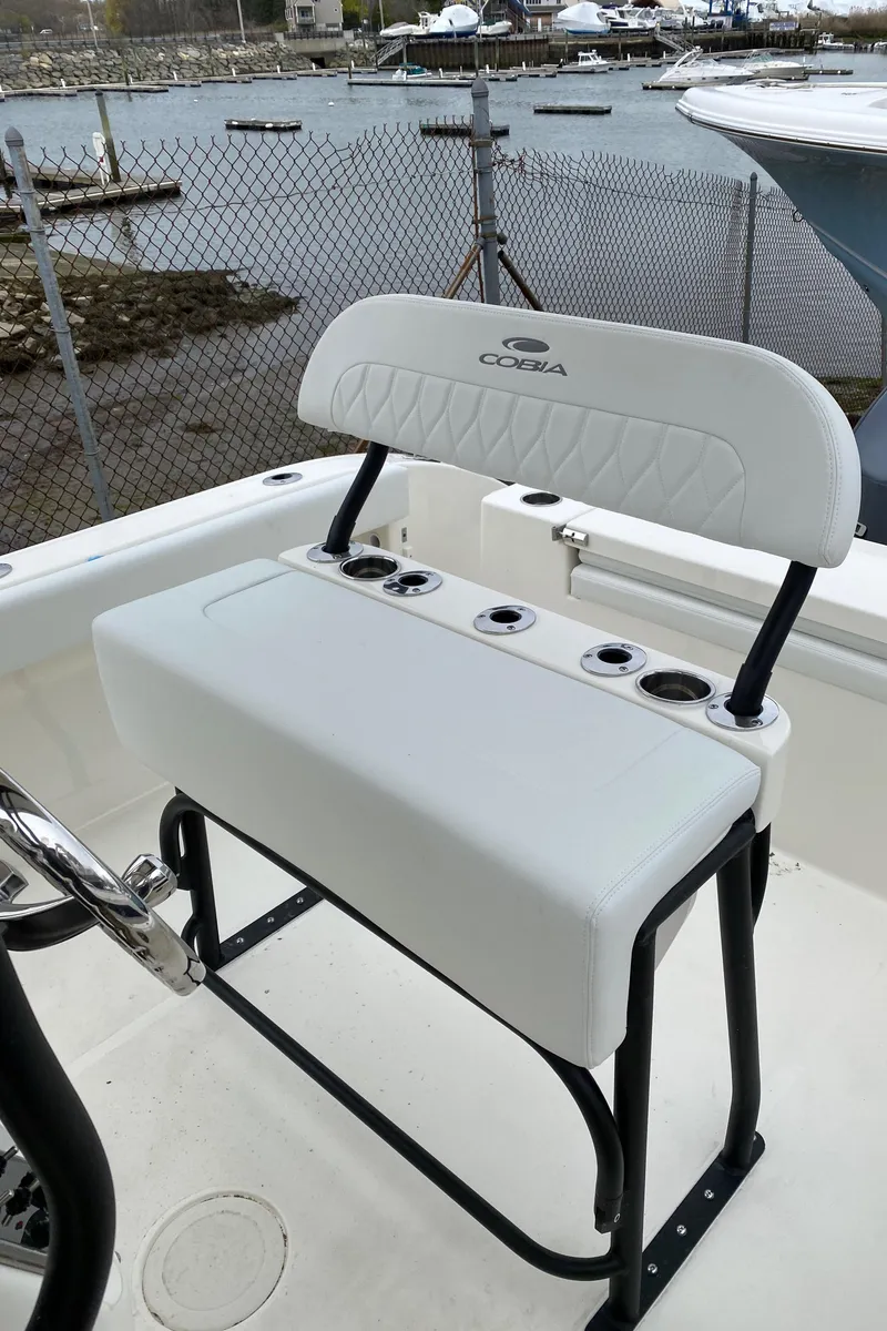 Slide: The Image of 2025 Cobia 220 boat seating with rod holders, docked by a chain-link fence. - 14