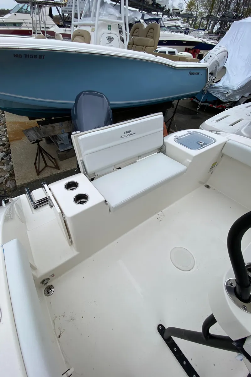 Slide: The Image of 2025 Cobia 220 boat interior with seating and cup holders, docked alongside other boats. - 6