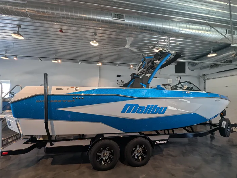 The Image of 2025 Malibu Wakesetter 25 LSV boat in showroom, blue and white design, on trailer. - 0