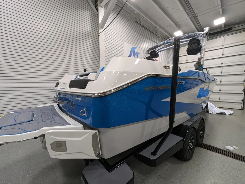 Slide: The Image of 2025 Malibu Wakesetter 25 LSV boat in showroom, blue and white design, on trailer. - 3