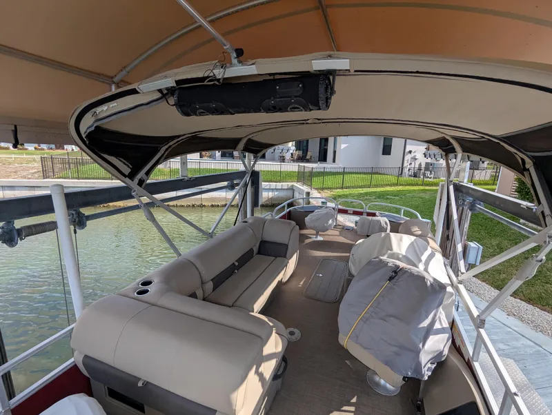 Slide: The Image of 2021 Sun Tracker Fishin' Barge 22 DLX interior with seating and canopy on a calm waterway. - 9