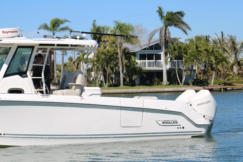 Slide: The Image of 2022 Boston Whaler 330 Outrage boat on water, surrounded by palm trees and a house. - 2