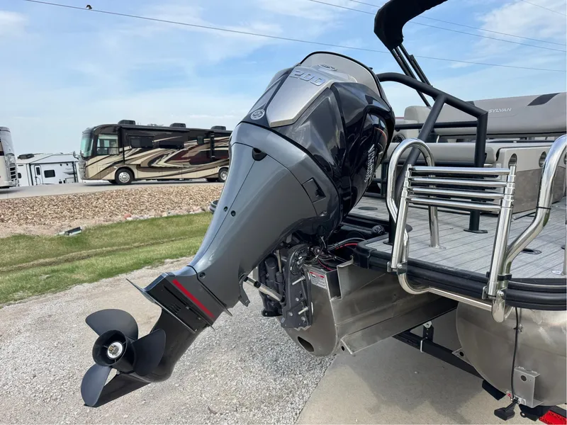 Slide: The Image of 2023 Sylvan L5 DLZ Bar pontoon boat with powerful outboard motor, parked near RVs. - 13