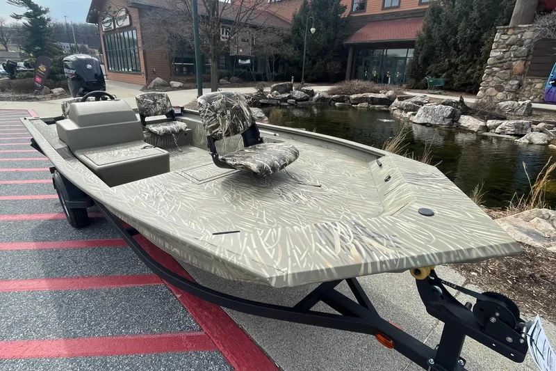 Slide: The Image of 2025 Tracker Grizzly 1754 SC boat with camouflage design, displayed outdoors near a pond. - 2