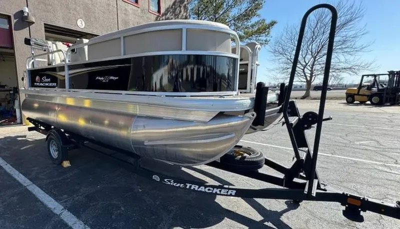 Slide: The Image of 2025 Sun Tracker Party Barge 16 DLX pontoon boat on trailer, parked outdoors. - 3