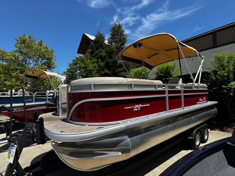 The Image of 2025 Sun Tracker Party Barge 22 DLX pontoon boat with canopy, parked outdoors. - 0