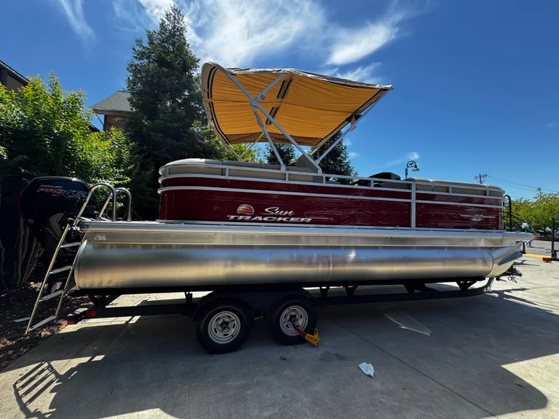 Slide: The Image of 2025 Sun Tracker Party Barge 22 DLX pontoon boat on trailer, parked outdoors. - 2