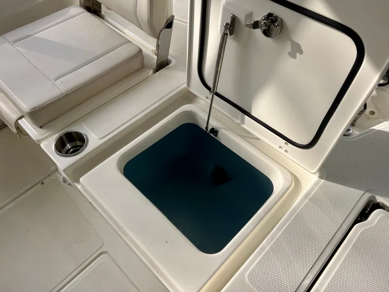 Slide: The Image of 2025 Boston Whaler 250 Dauntless livewell, open lid, white interior, cup holder nearby. - 9