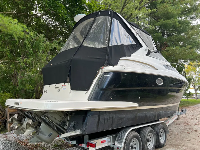 Slide: The Image of 2013 Regal 30 Express boat on trailer, black and white exterior, surrounded by trees. - 2