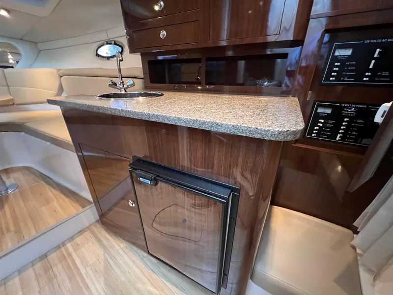Slide: The Image of 2013 Regal 30 Express yacht interior with kitchenette, featuring wood cabinetry and compact fridge. - 26