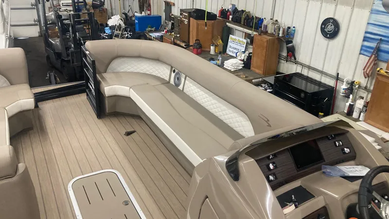 Slide: The Image of 2022 Bennington 25 LSB boat interior with beige seating and modern dashboard in a workshop. - 11