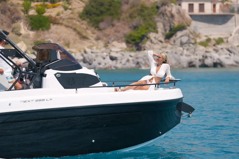 Slide: The Image of 2025 Ranieri NEXT 255 LX boat with woman relaxing on deck in scenic coastal waters. - 16