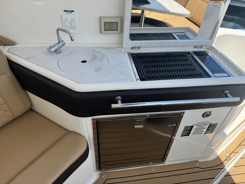 Slide: The Image of 2021 Sea Ray Sundancer 320 Coupe Outboard boat kitchenette with sink, grill, and seating. - 16