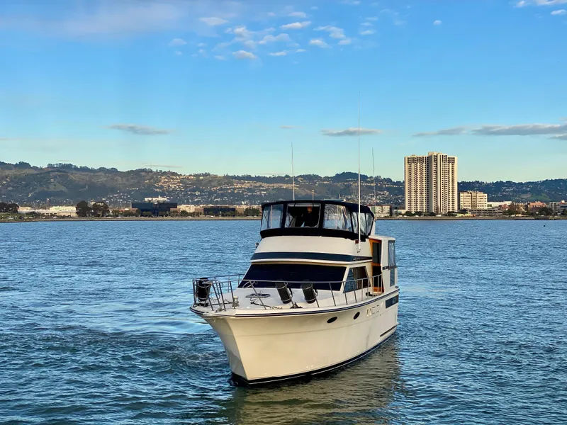 Slide: The Image of 1988 Californian Sundeck Motoryacht cruising on a scenic waterway with city skyline backdrop. - 3