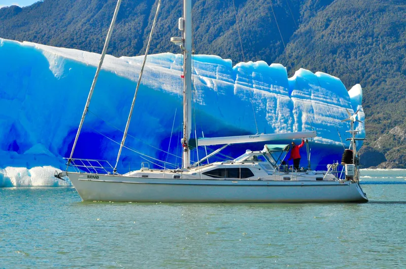 Slide: The Image of Roger Hill 2000 Cruising Cutter sailing near a vibrant blue glacier in a scenic landscape. - 5