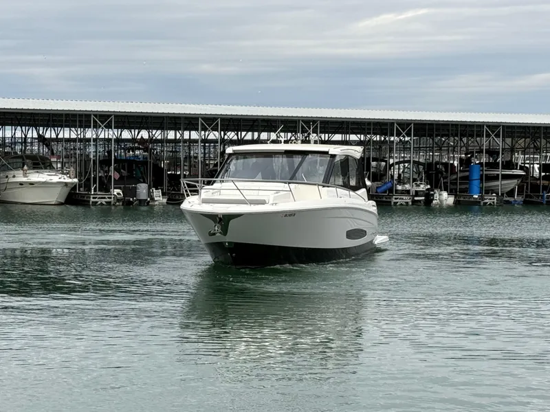 Slide: The Image of 2023 Regal 360 Grande Coupe boat on calm water near a marina. - 2