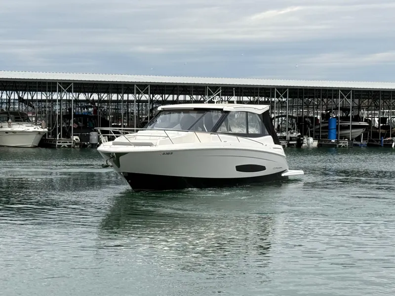 Slide: The Image of 2023 Regal 360 Grande Coupe boat on calm water near a marina. - 3