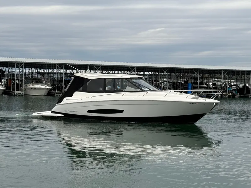 Slide: The Image of 2023 Regal 360 Grande Coupe yacht on calm water near a marina. - 7