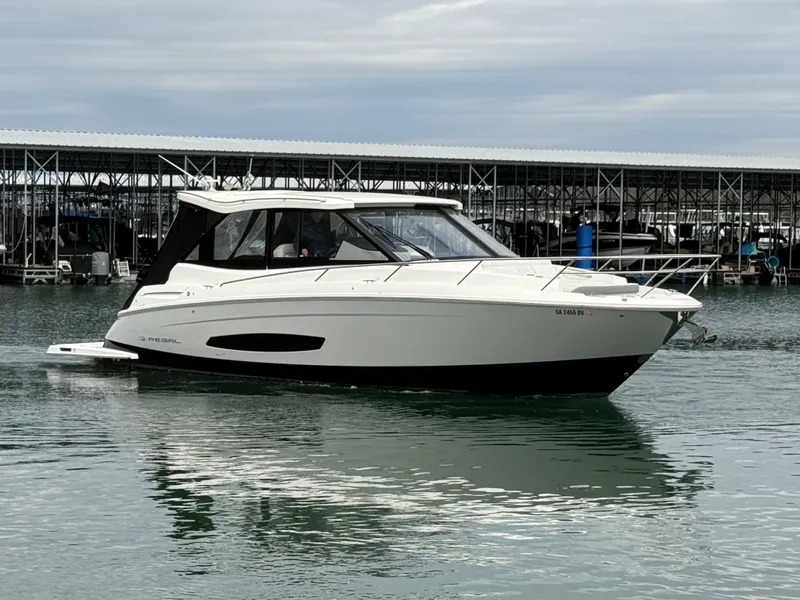 Slide: The Image of 2023 Regal 360 Grande Coupe boat on calm water near a marina. - 8