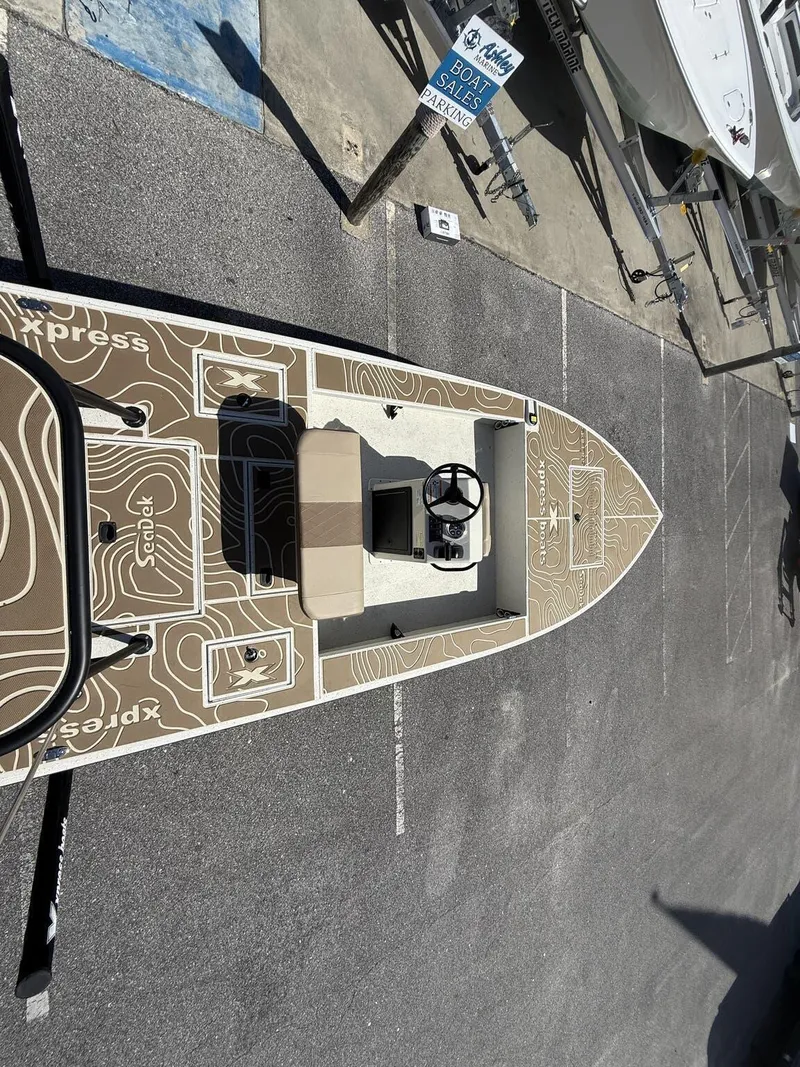 Slide: The Image of 2025 Xpress Skiff 185 boat with unique deck design, parked in sales area. - 9