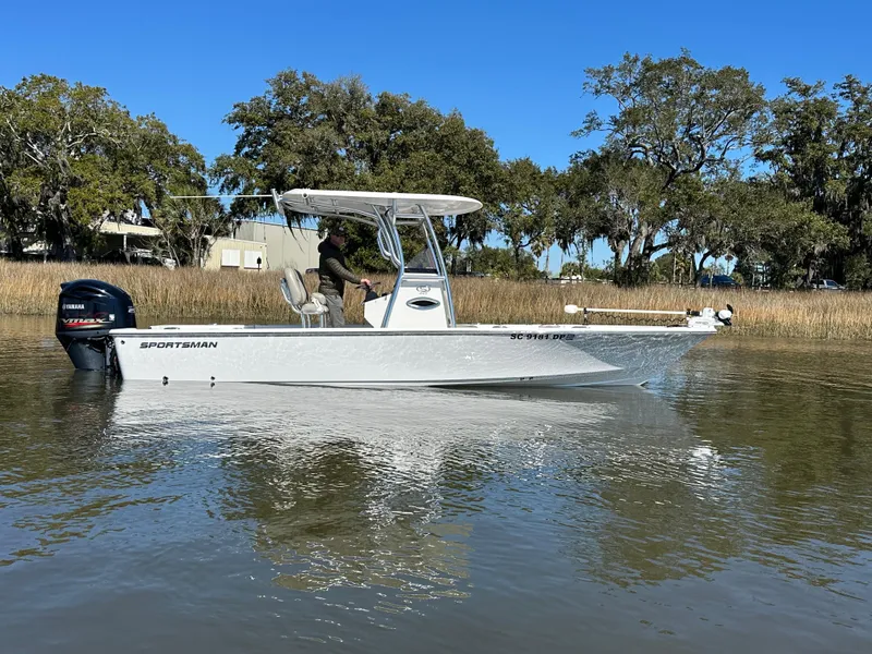 Slide: The Image of 2021 Sportsman Masters 247 Bay Boat on calm water, surrounded by trees. - 2